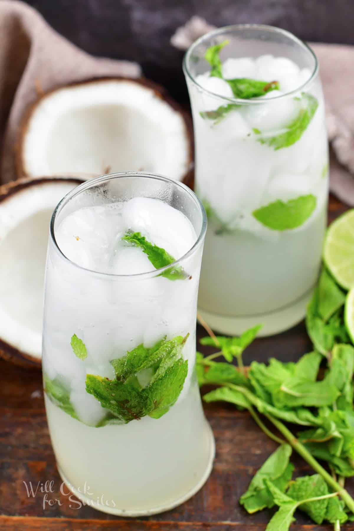 two glasses filler with white and green coconut mojito cocktails and halved coconut.