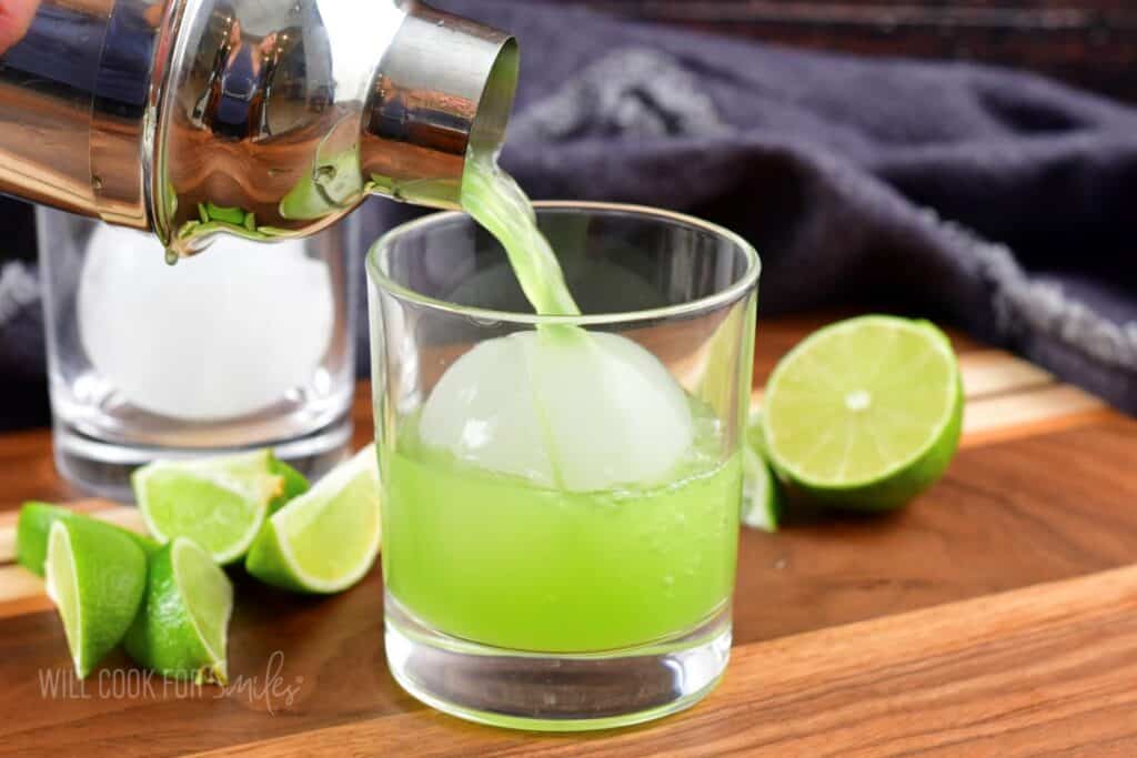pouring the cucumber cocktail over ice in a glass.