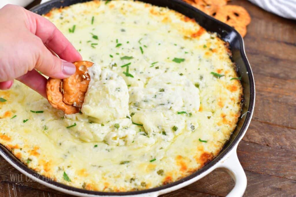 closeup of scooping cheese dip with a pretzel chip.