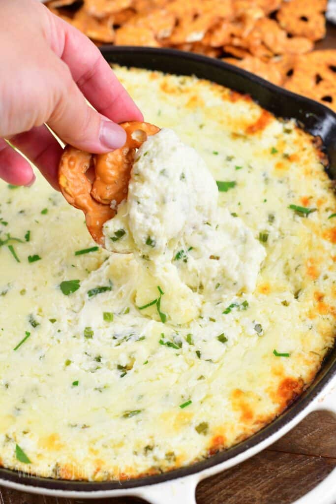 dipping pretzel chip into the baked cheese dip.