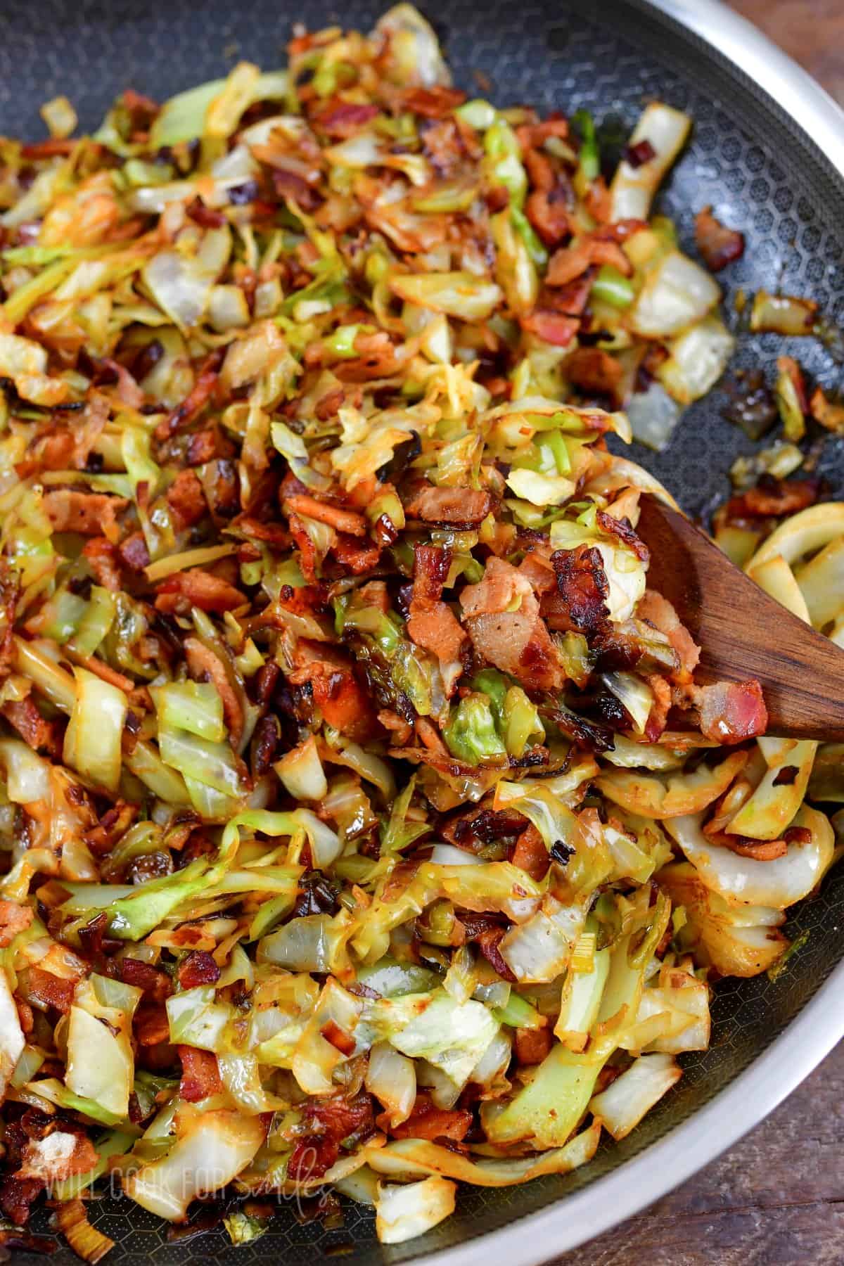 scooping out some fried cabbage from a pan with a spoon.