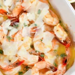 closeup of pink shrimp baked in butter in white dish.