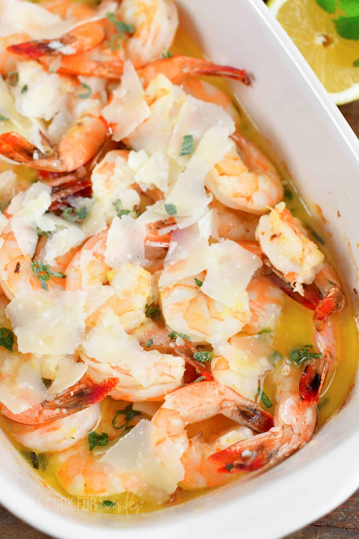 closeup of pink shrimp baked in butter in white dish.