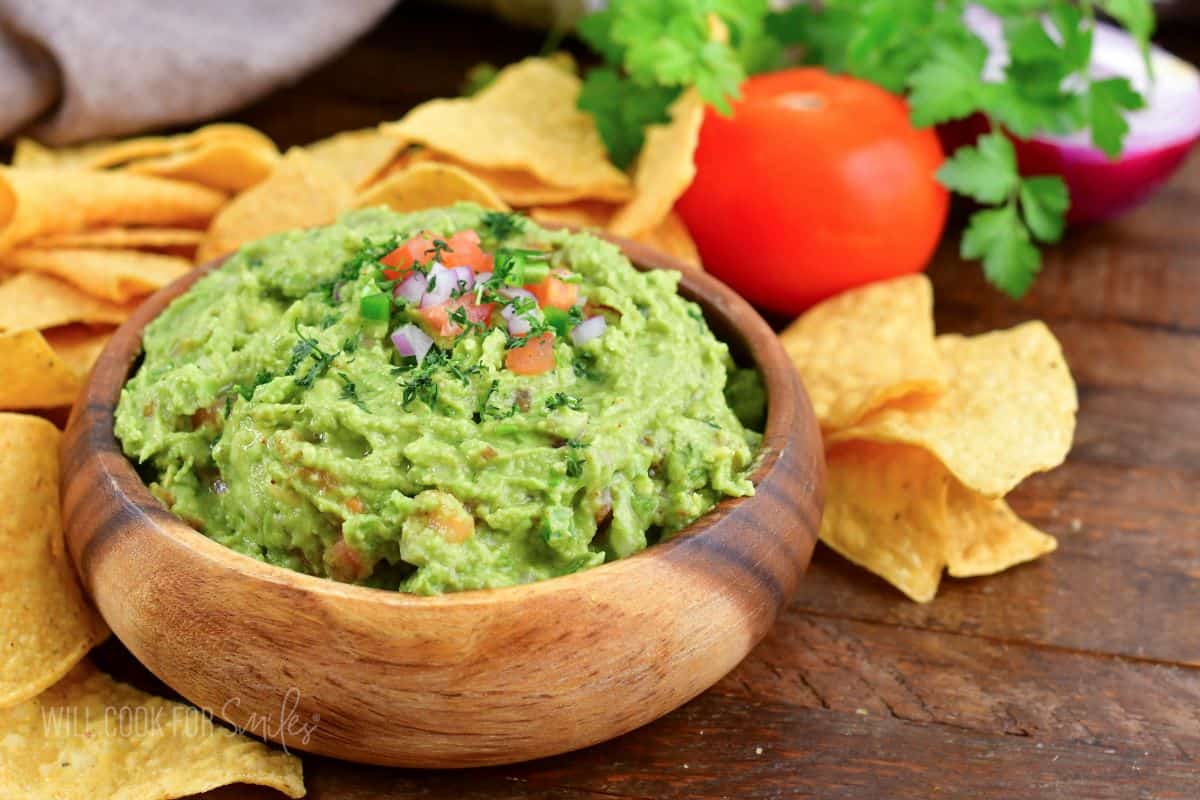 guacamole in a wooden bowl with chips around it.
