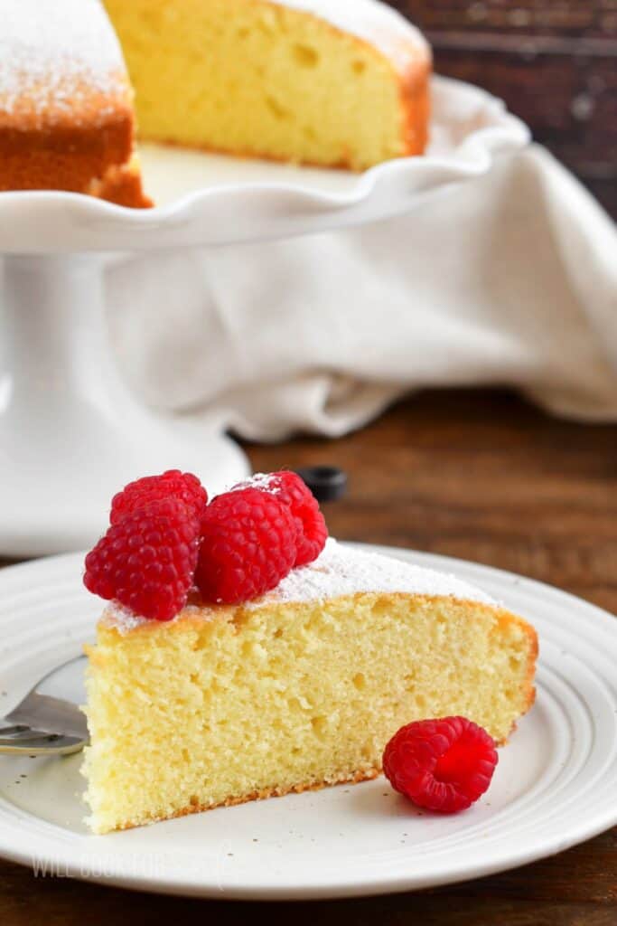 Slice of Irish cake on a plate with raspberries on top.