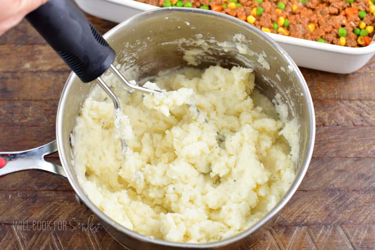 mashing the mashed potatoes in a silver pot.