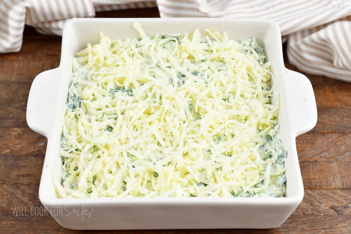 spinach dip in the baking dish topped with shredded cheese.