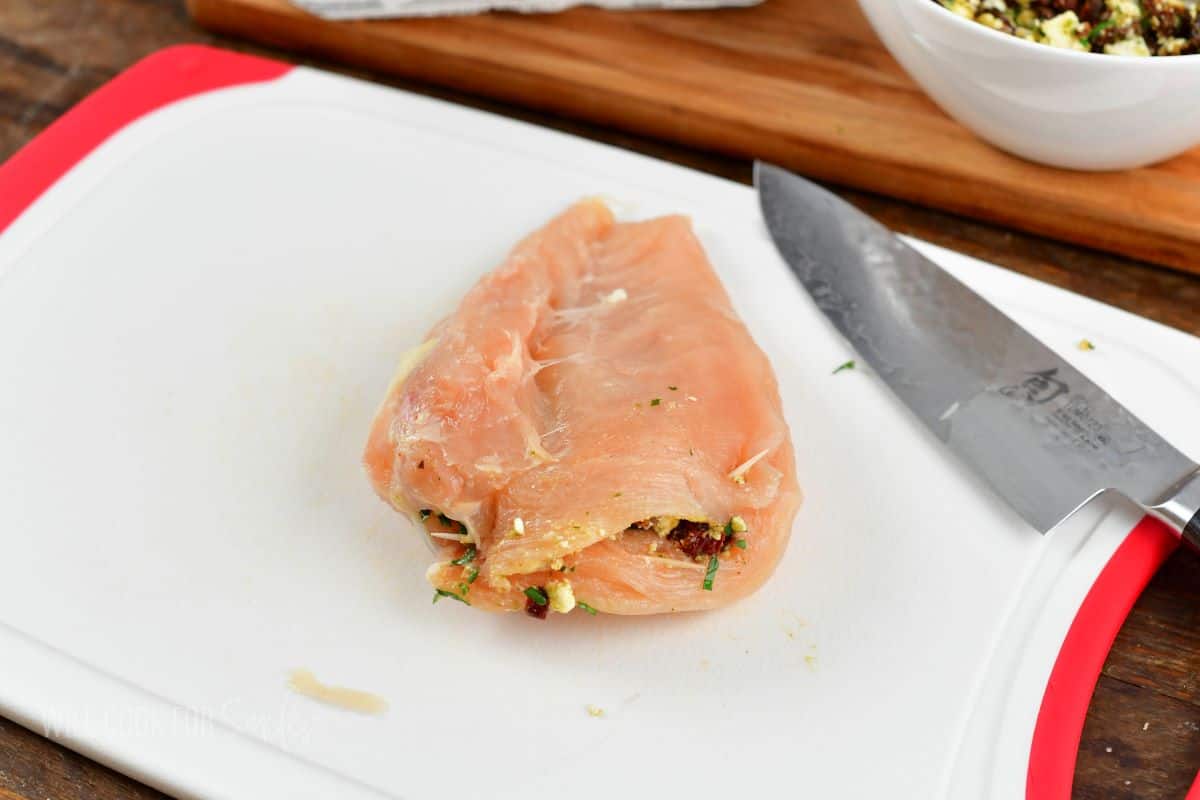 stuffed chicken breast closed with toothpicks on cutting board.
