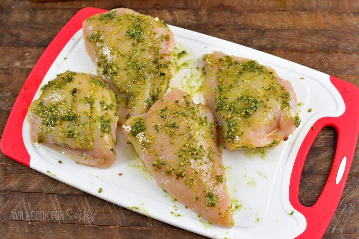 four pesto rubbed stuffed chicken breasts in a cutting board.