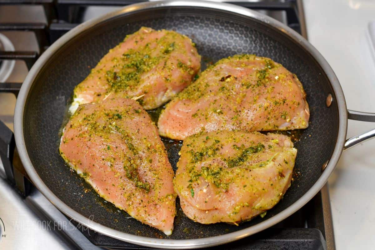 starting to cook pesto rubbed chicken breasts in a pan.