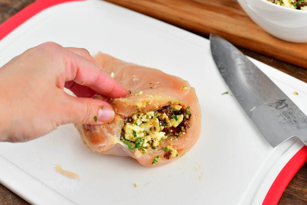 stuffing a raw chicken breast with tomato feta and pesto filling.