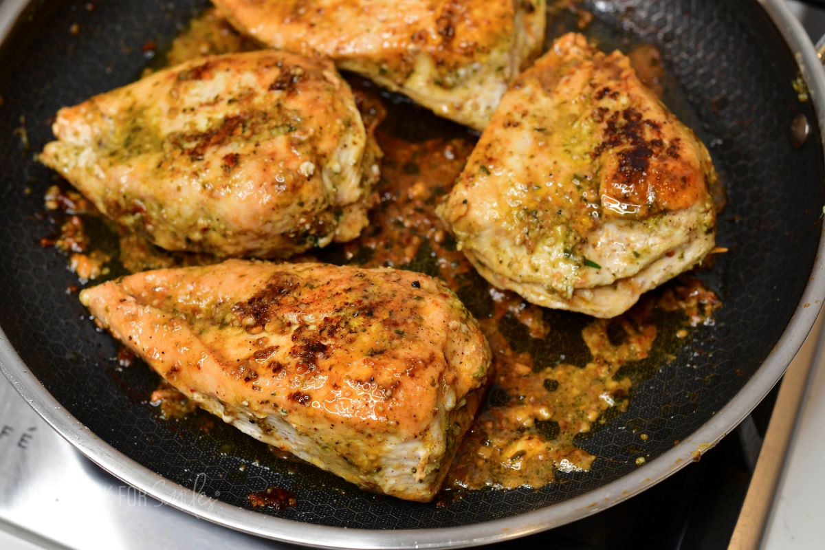 four stuffed chicken breasts cooking in a pan.