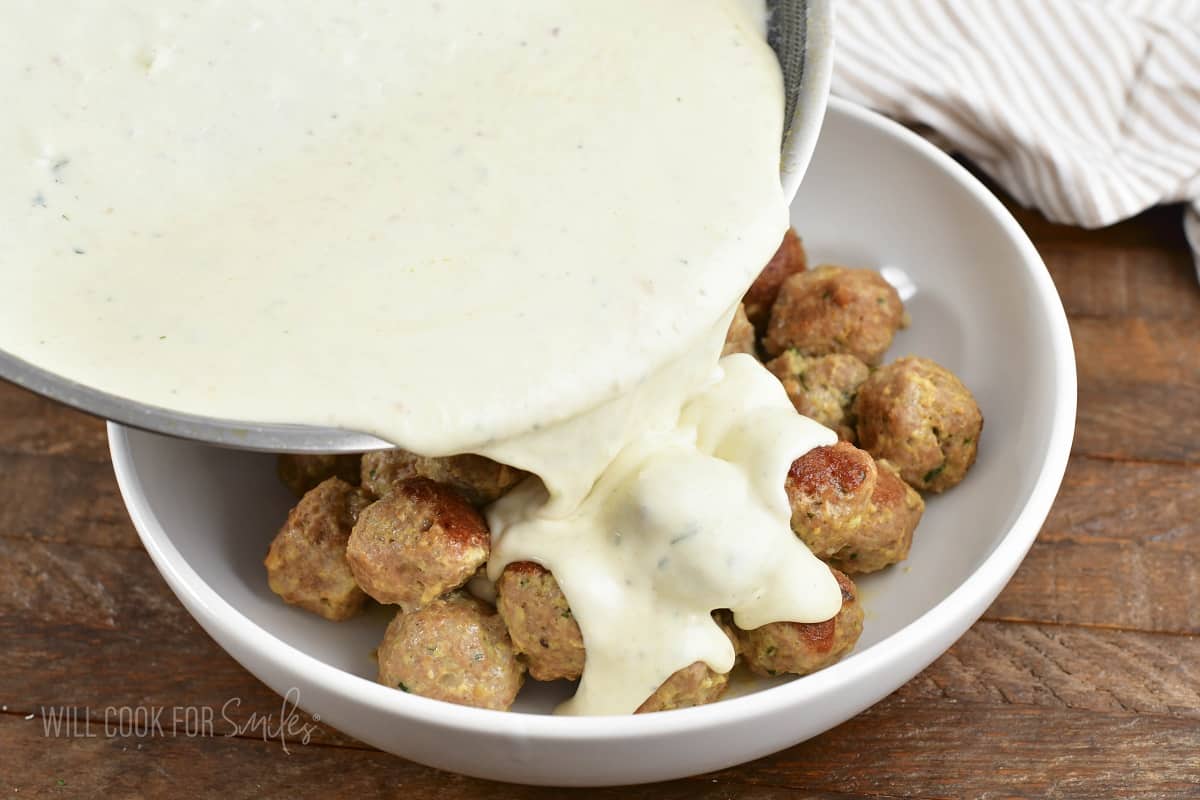 pouring parmesan cream sauce over the meatballs.