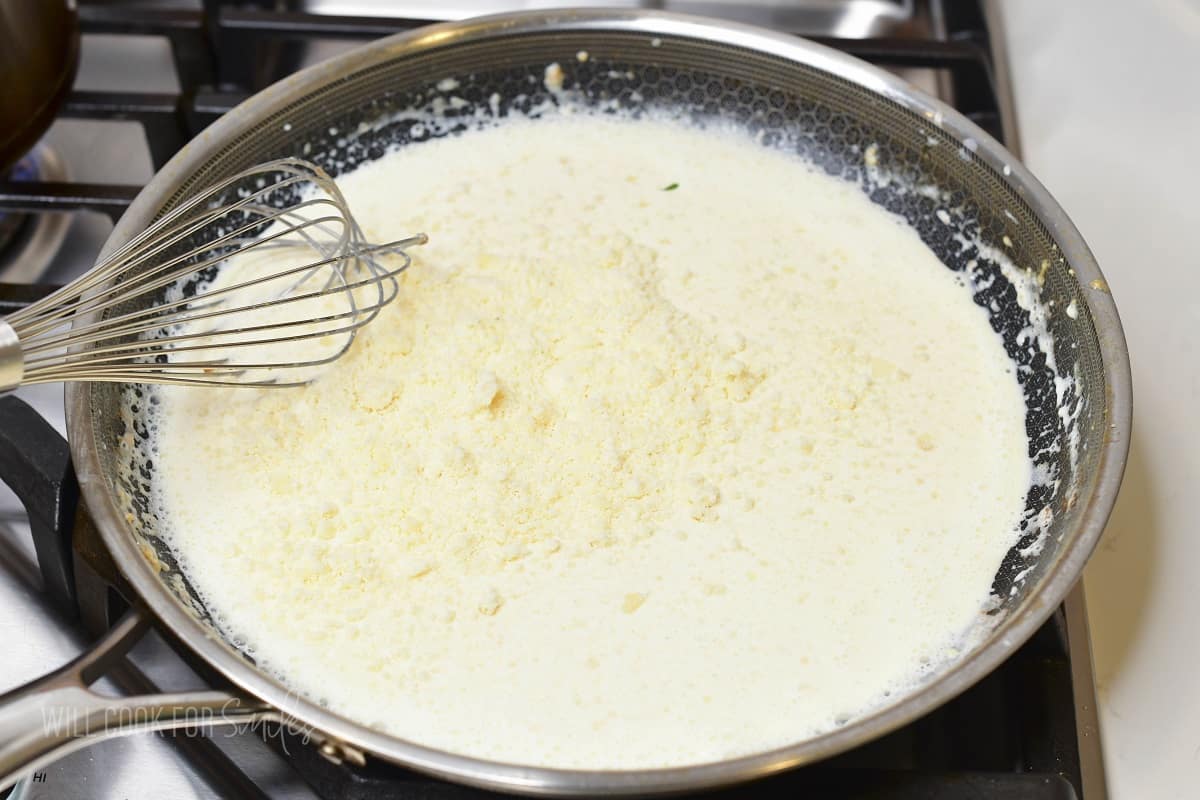 adding grated parmesan to cream sauce.