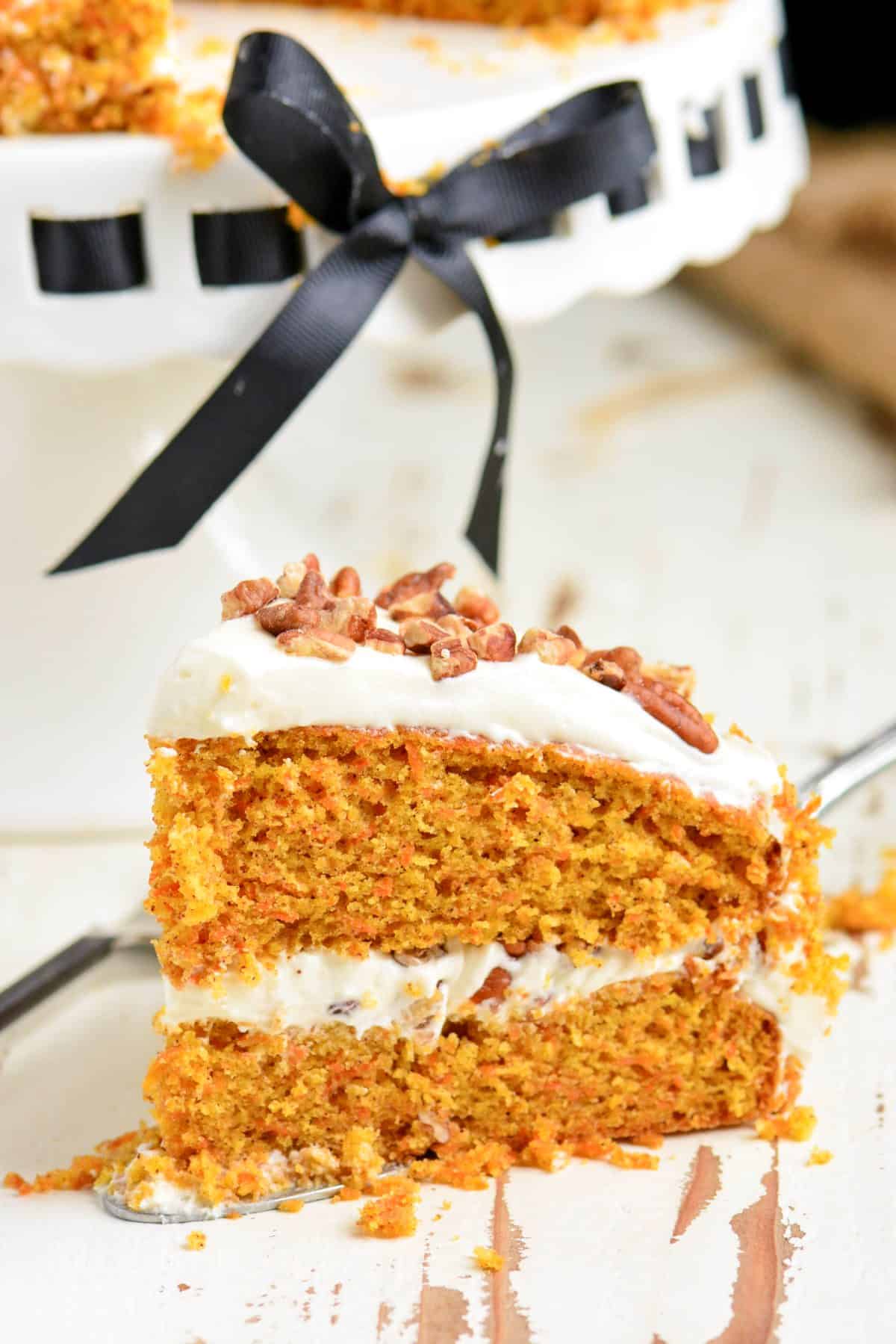 a slice of carrot cake on a silver spatula next to the cake stand.