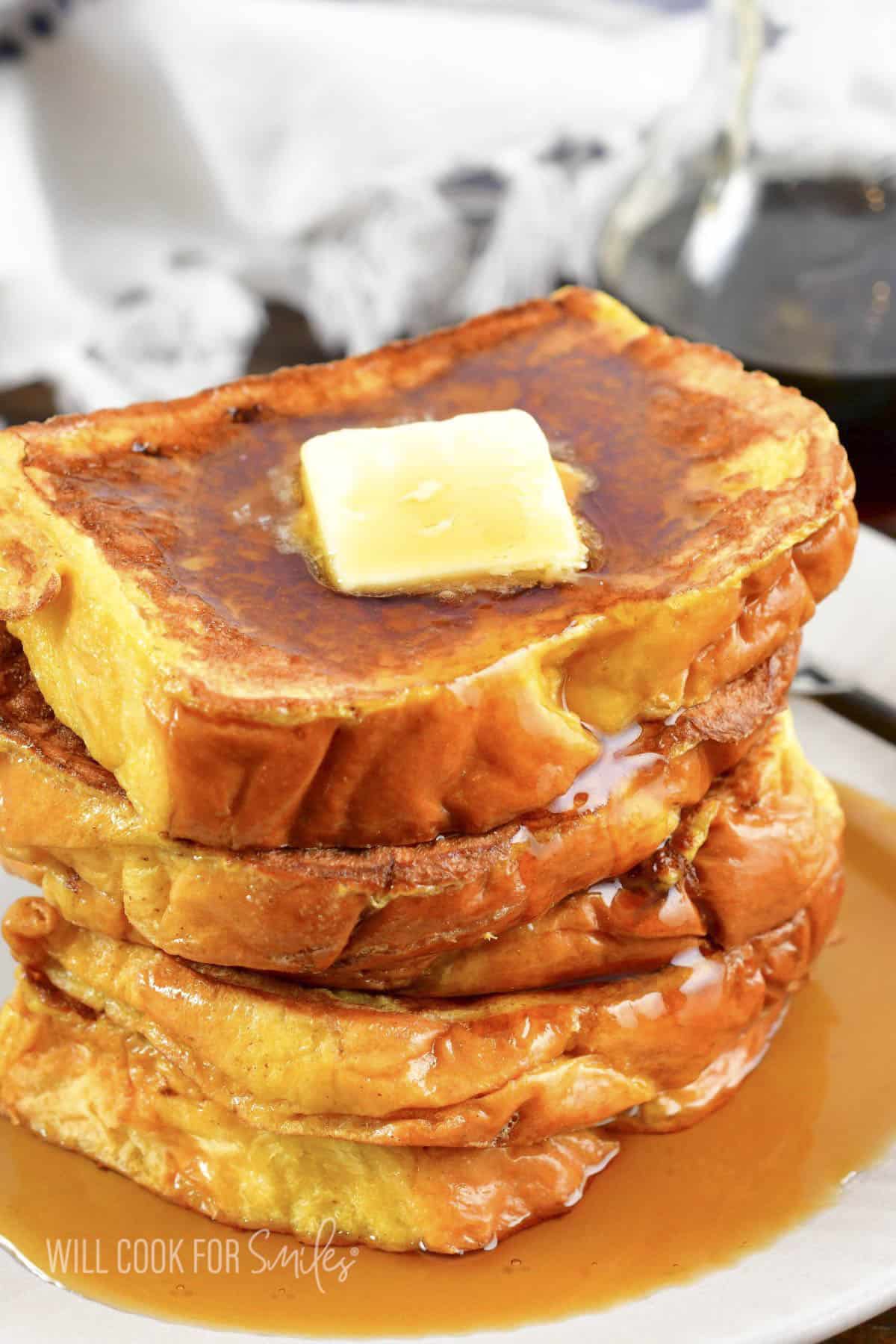stacked French Toast slices with butter and maple syrup on light plate.