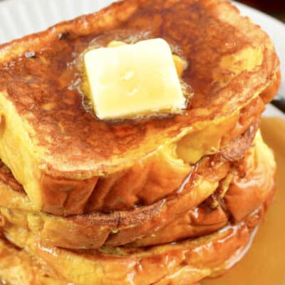 Several slices of French Toast stacked with butter and syrup on top.