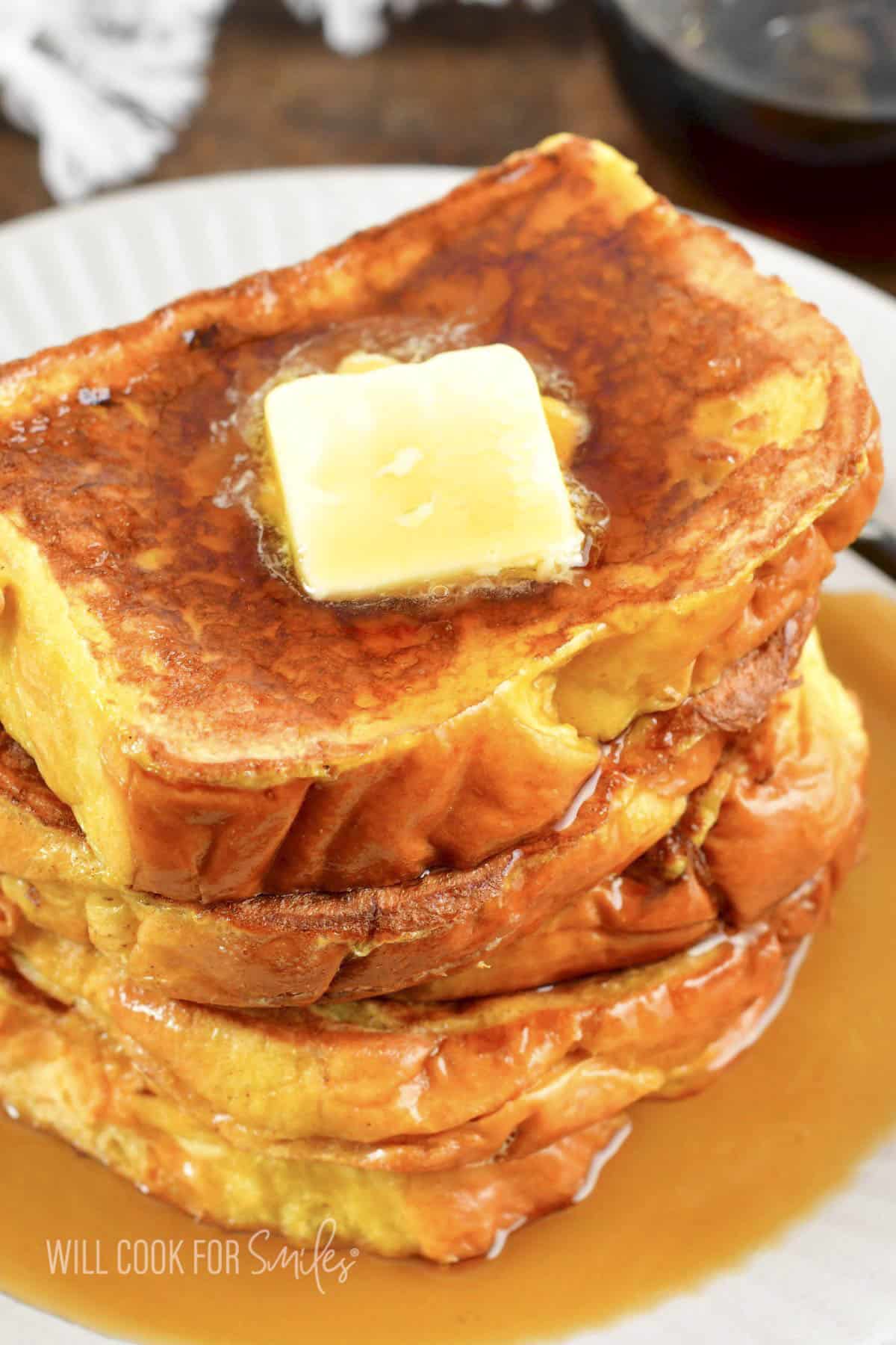 Several slices of French Toast stacked with butter and syrup on top.