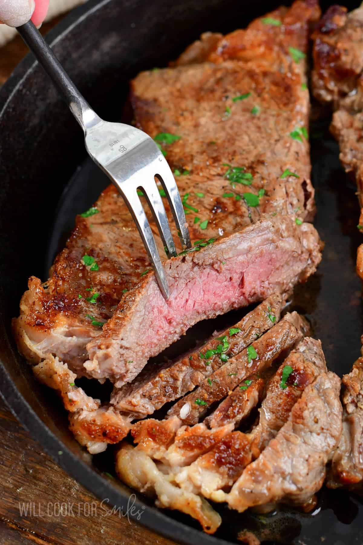 sliced steak in a skillet and holding a piece with a fork.