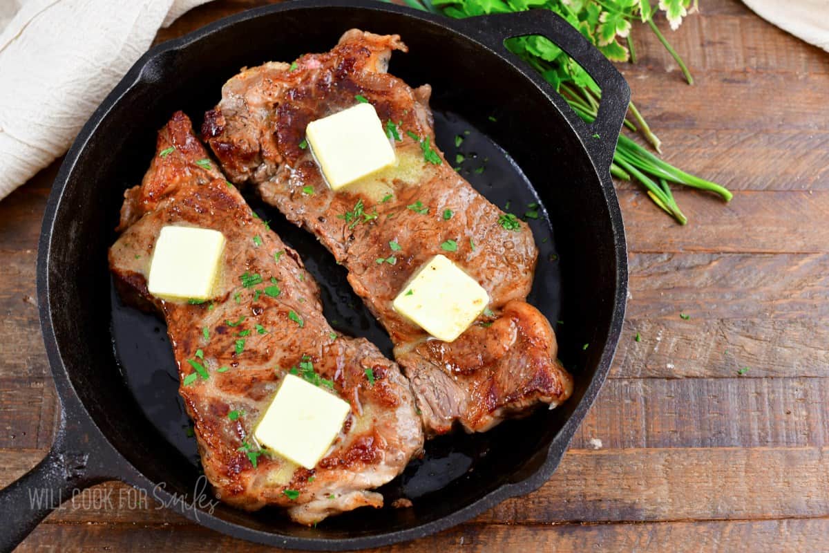 two oven cooked steaks in a black skillet with butter and parsley.