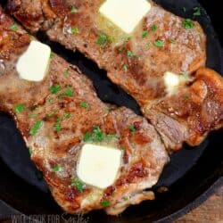 closeup of patrial two steaks topped with butter and parsley.