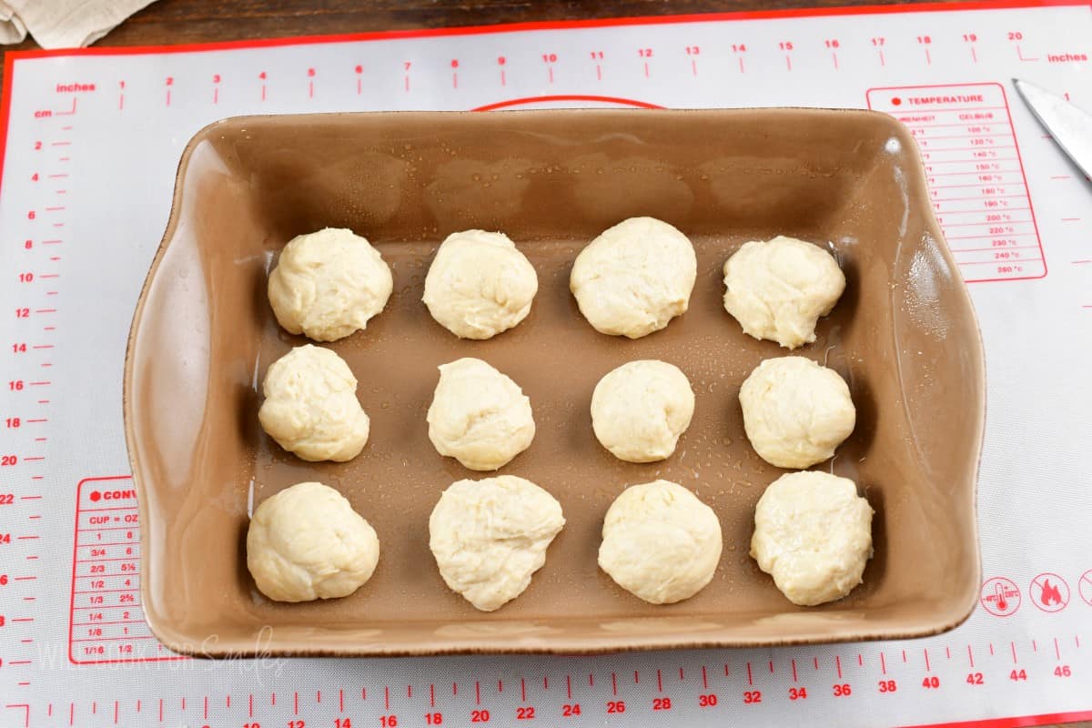 twelve pieces of dough lined up in the baking dish.