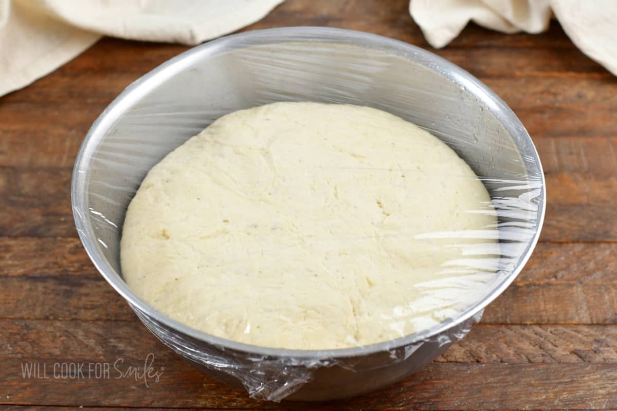 raised dough in a metal bowl with plastic cover.