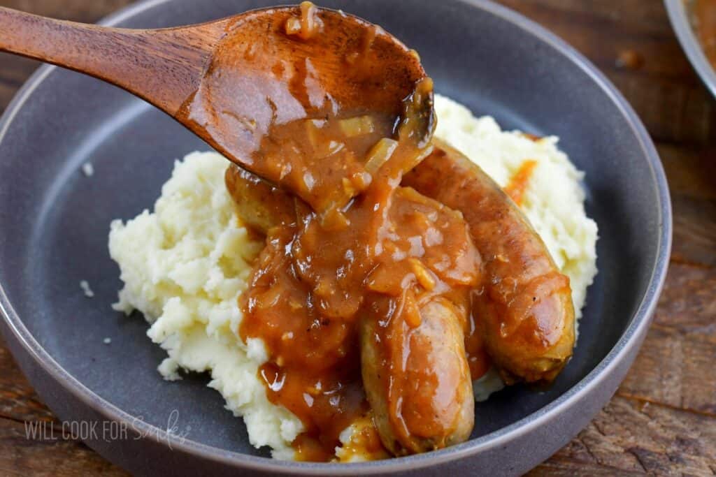 adding gravy on top of the sausages and mashed potatoes.