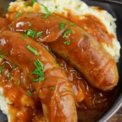 closeup of sausages in gravy over mashed potatoes.