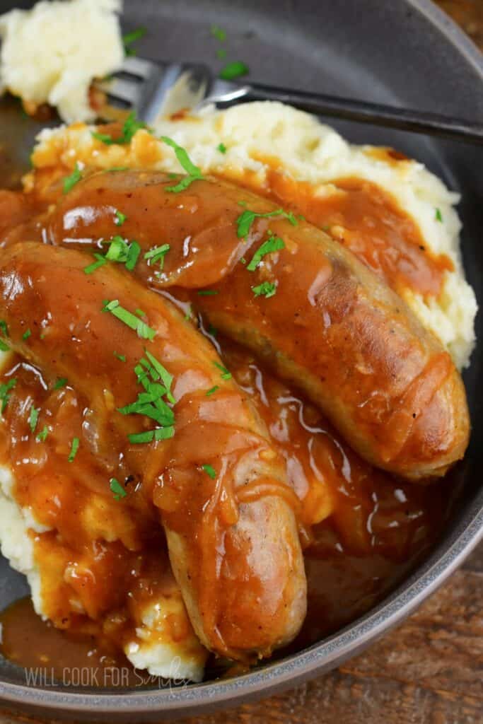 closeup of sausages in gravy over mashed potatoes.