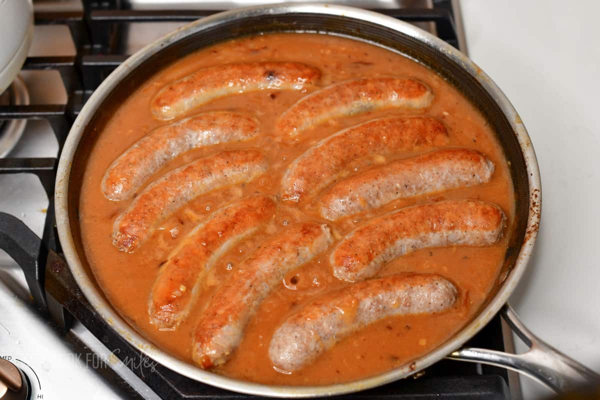 sausages simmering in gravy in the pan.