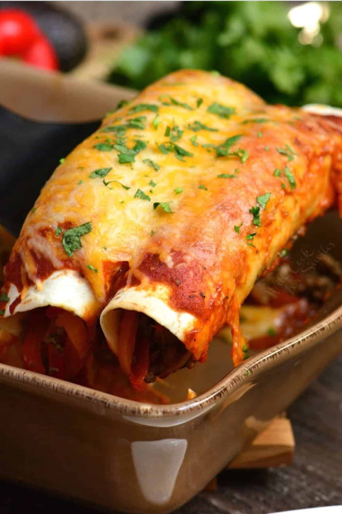 pulling out two cheesy enchiladas from the baking dish.
