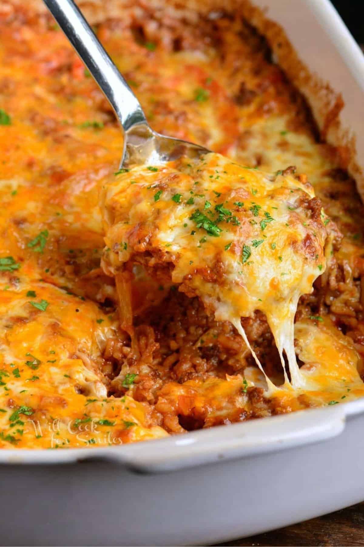 Scooping some cheesy casserole out of the white baking dish.