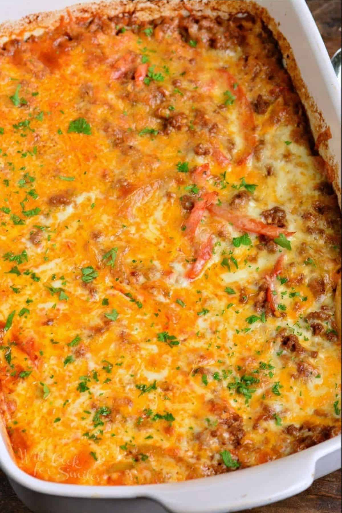 baked enchilada casserole topped with cheese and cilantro on white baking dish.