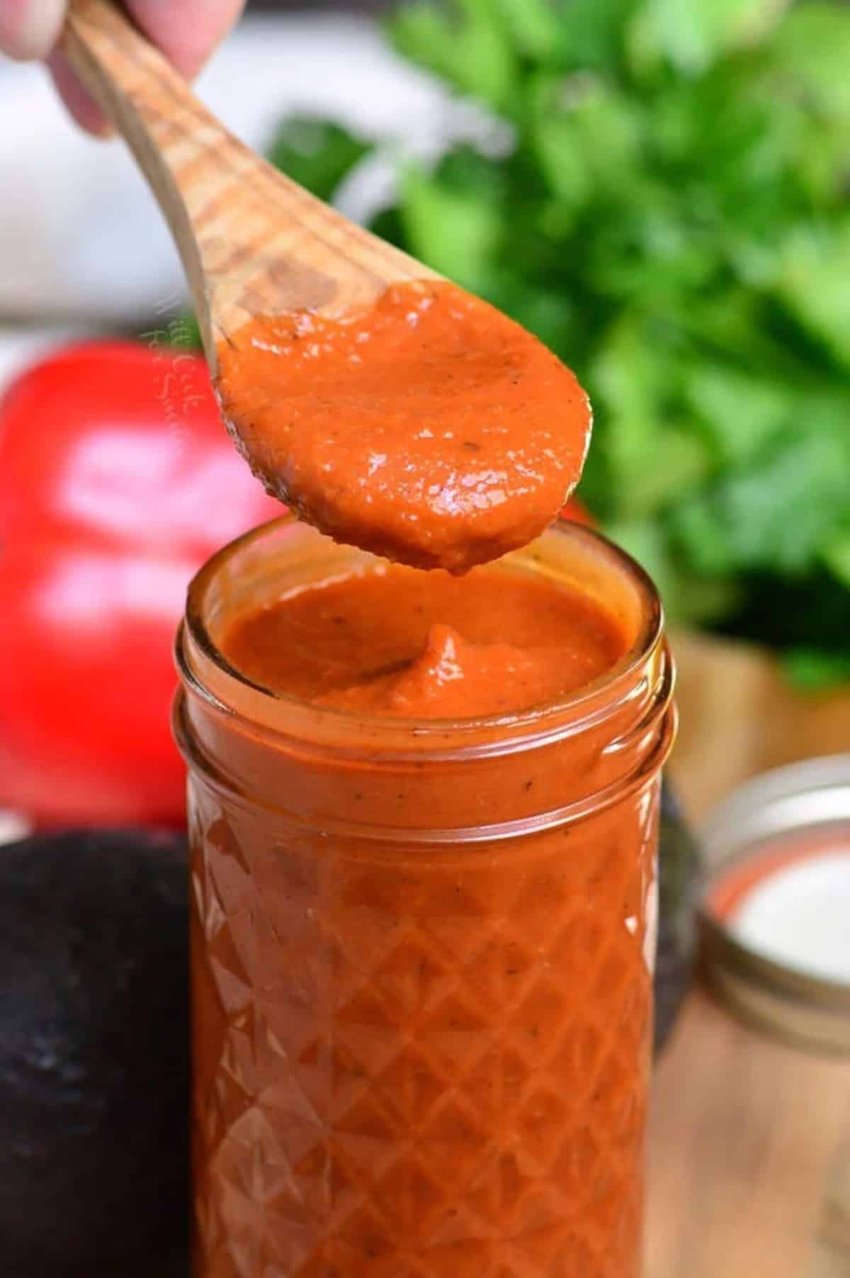 some enchilada sauce on a wooden spoon held over the glass jar of sauce.