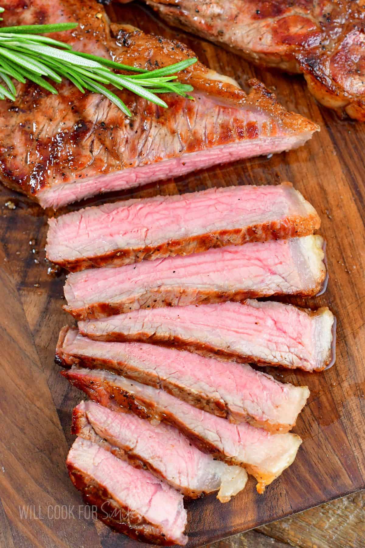 several thin slices of steak next to remaining steak on cutting board.