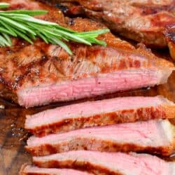 grilled steak with several thin slices cut off and rosemary sprig on top.