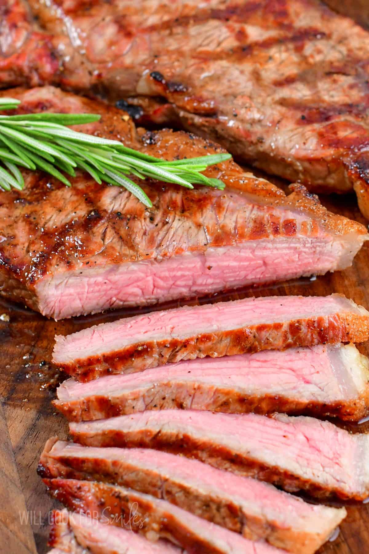 grilled steak with several thin slices cut off and rosemary sprig on top.