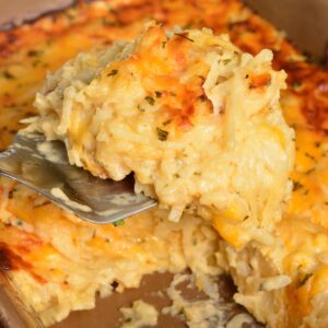 holding some scooped hashbrown casserole on a metal spatula over the dish.