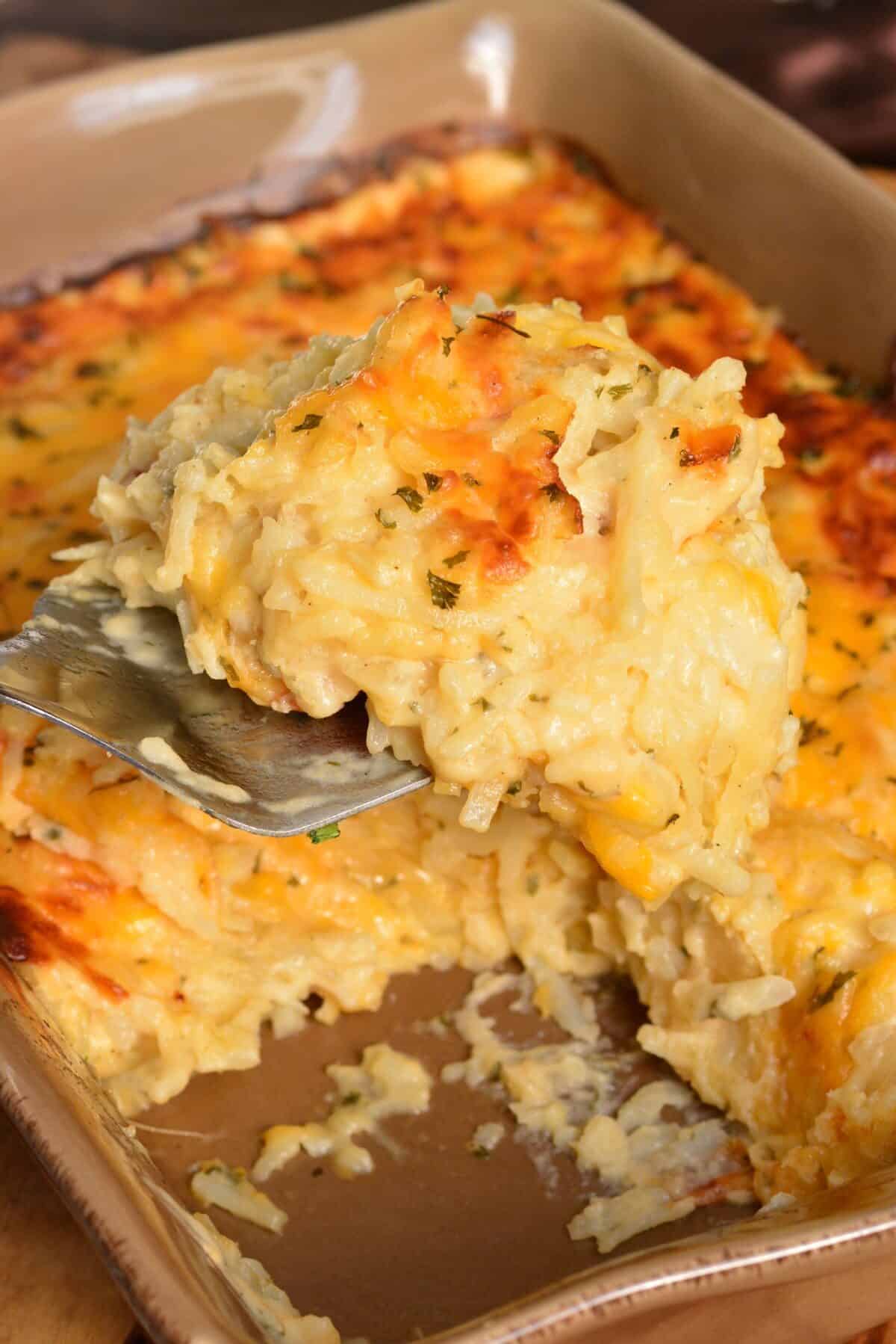 holding some scooped hashbrown casserole on a metal spatula over the dish.