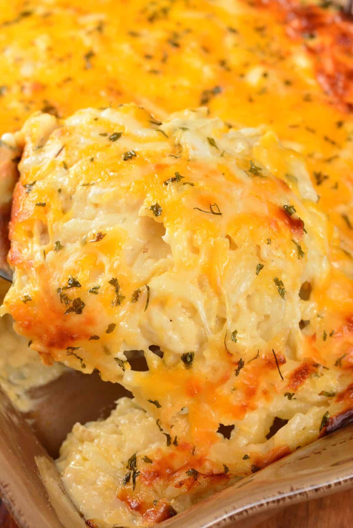 starting to scoop out cheesy potato casserole from the baking dish to show gooey cheese.