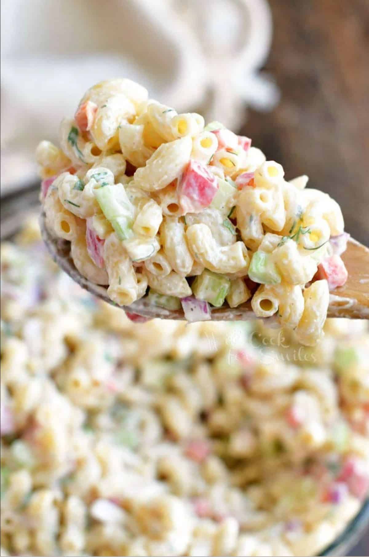 macaroni salad on a wooden spoon next to a bowl and a towel.