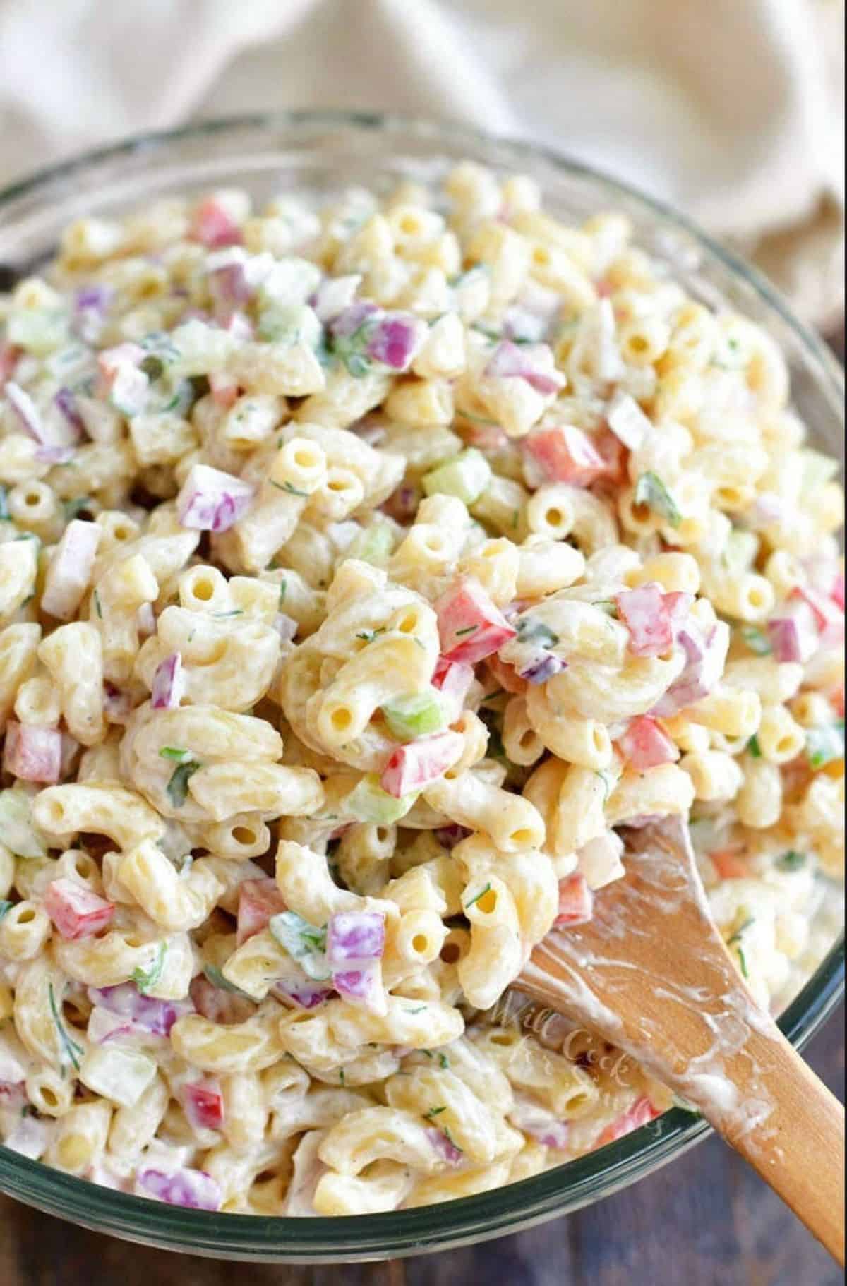 using a wooden serving spoon to scoop out some macaroni salad from a bowl.