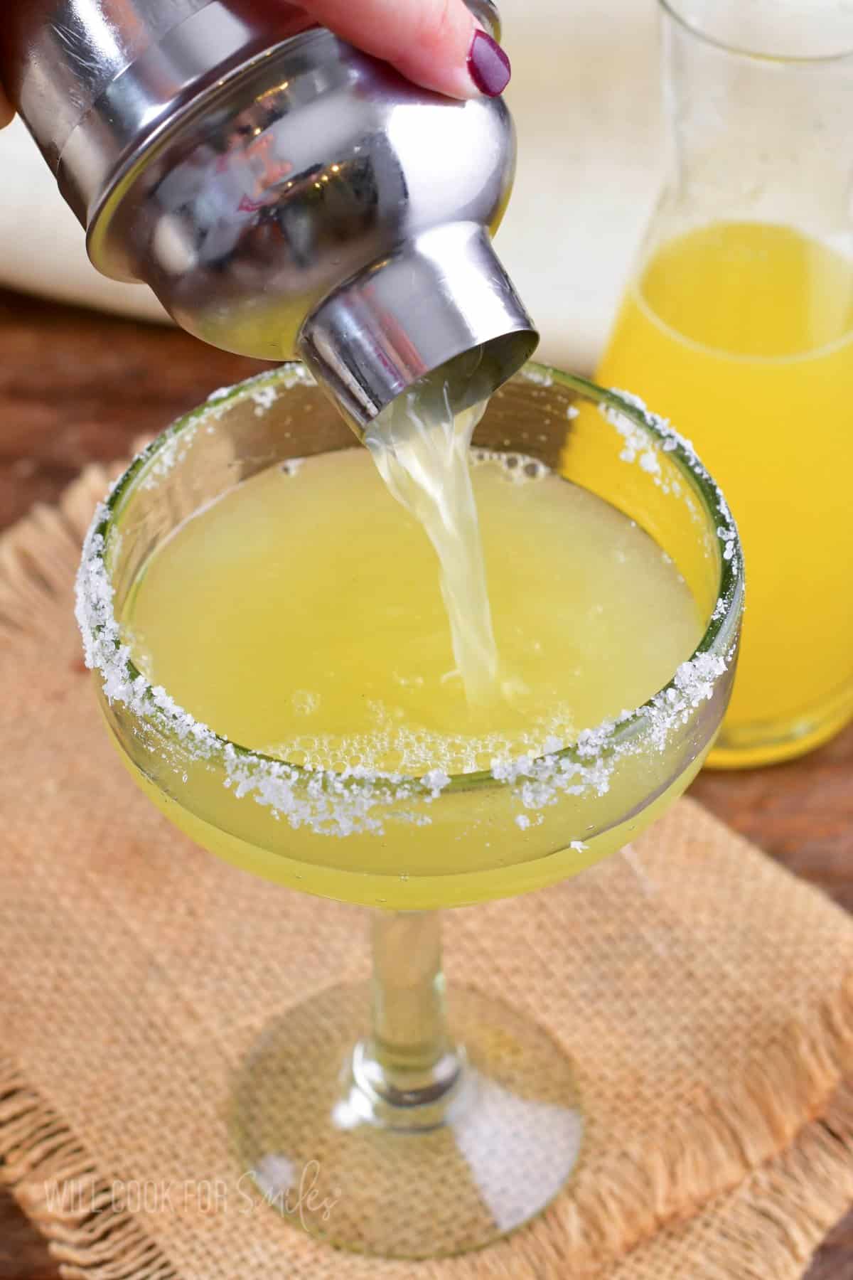 pouring a margarita from a shaker into a glass with salted rim.