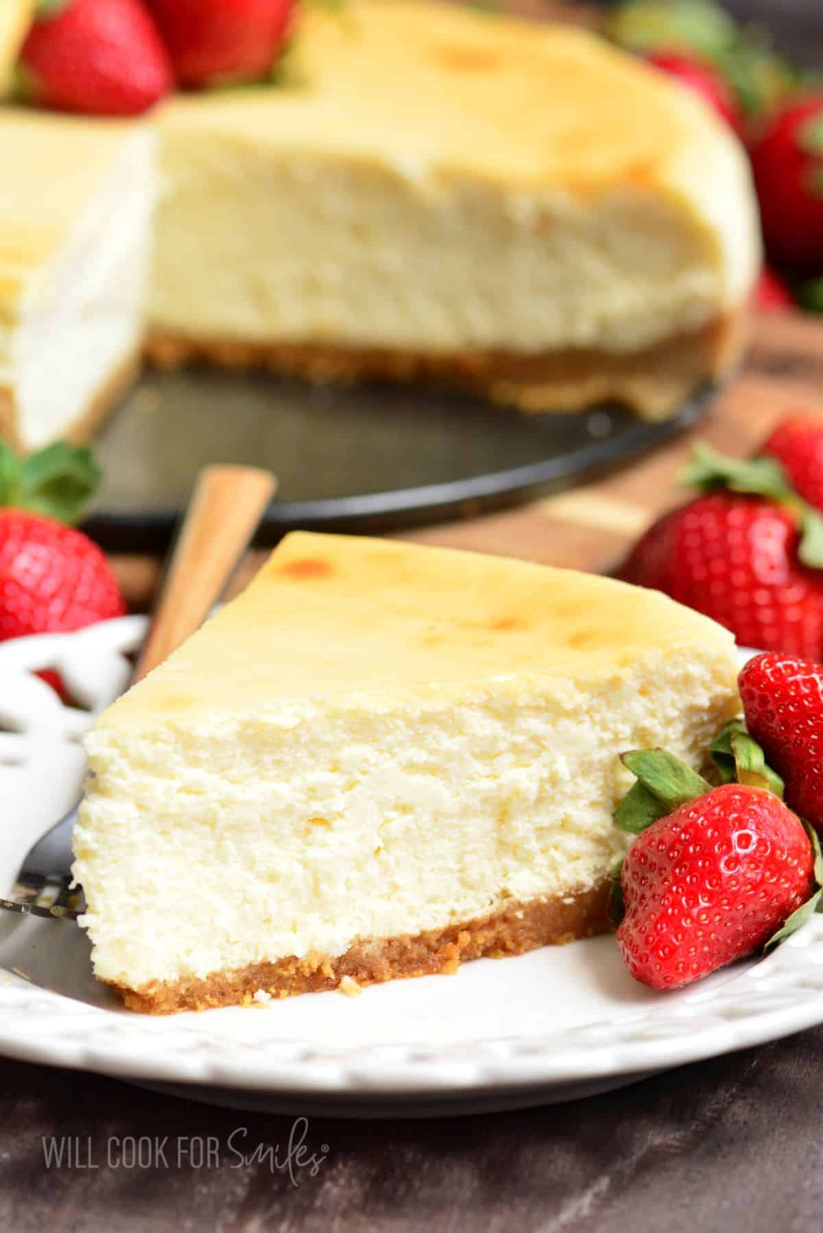 slice of NY cheesecake on a plate with strawberries and a fork.