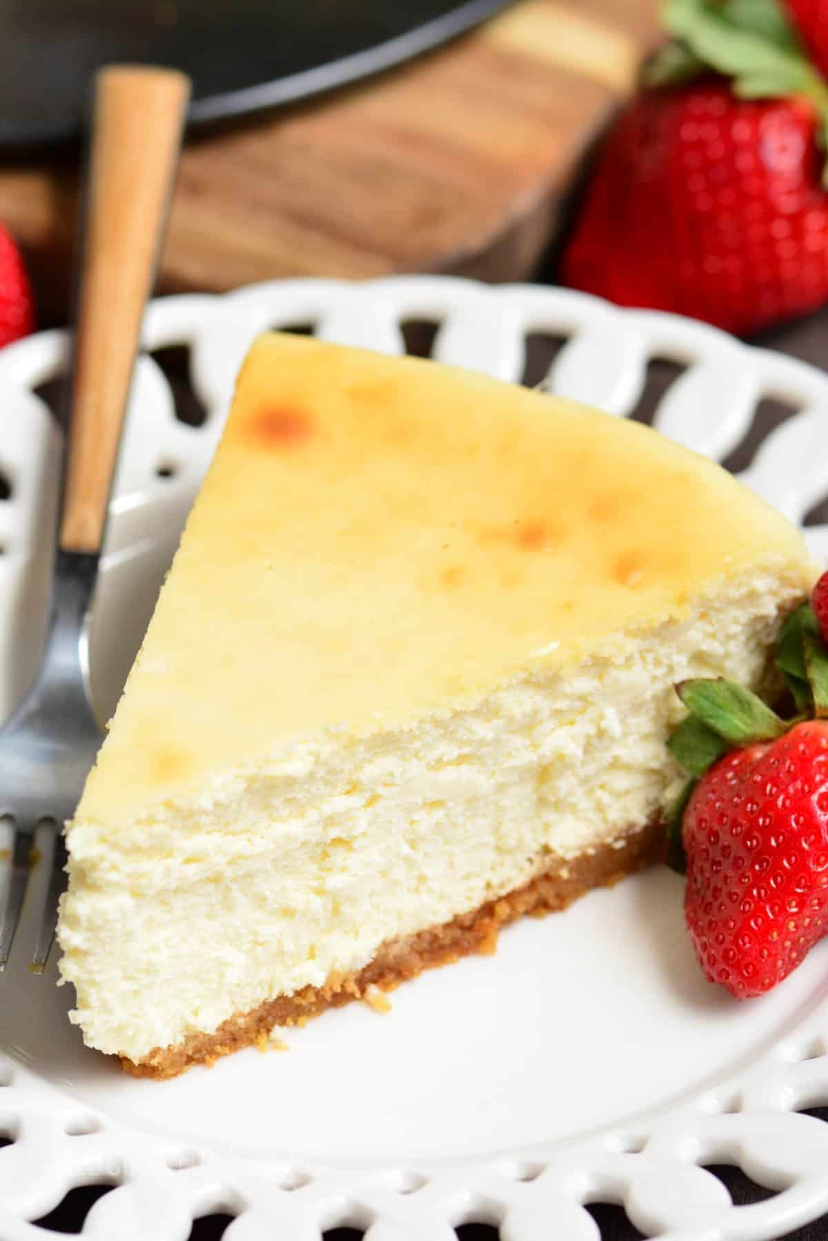 slice of classic cheesecake on a white plate with a fork and a strawberry.