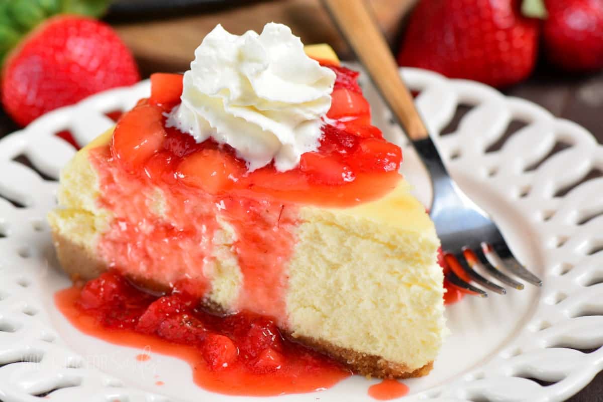 slice of classic cheesecake with strawberry topping and whipped cream on a plate.