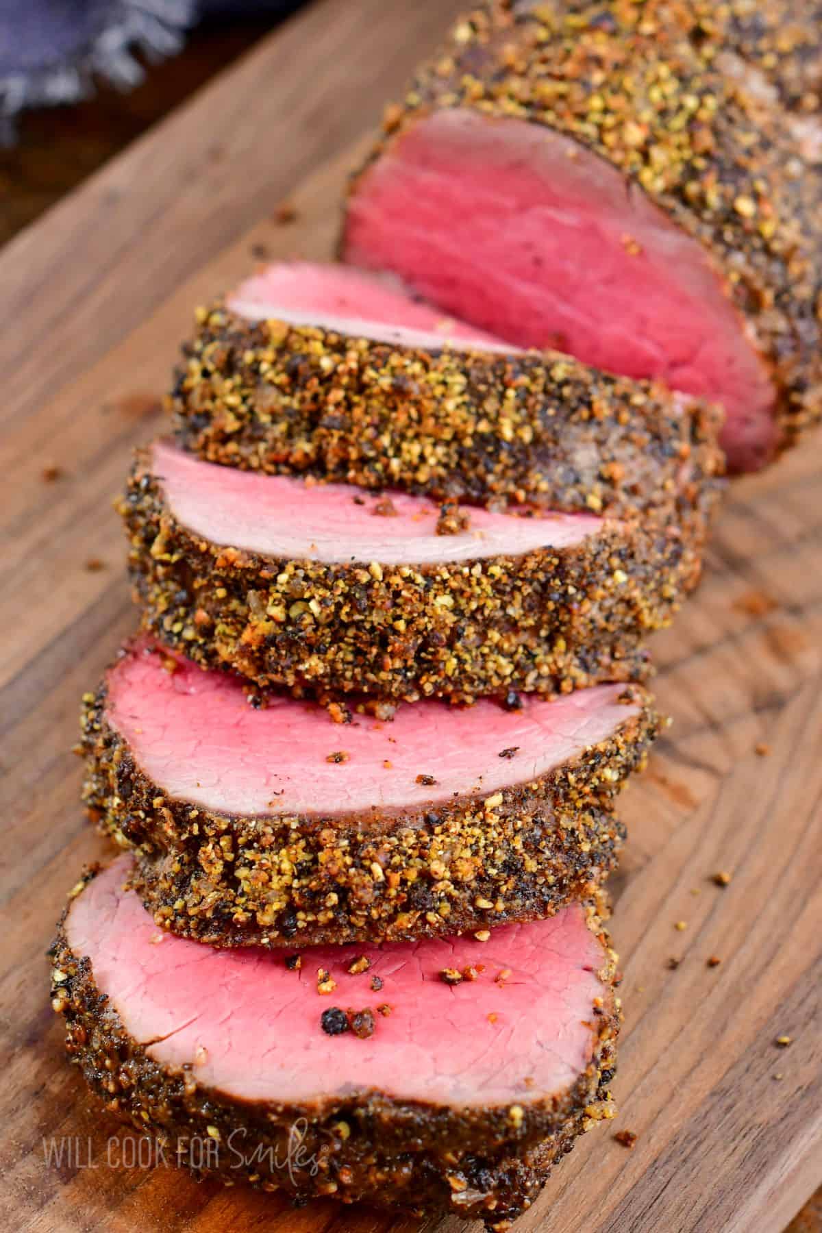 sliced beef tenderloin crusted in peppercorn seasoning on cutting board.