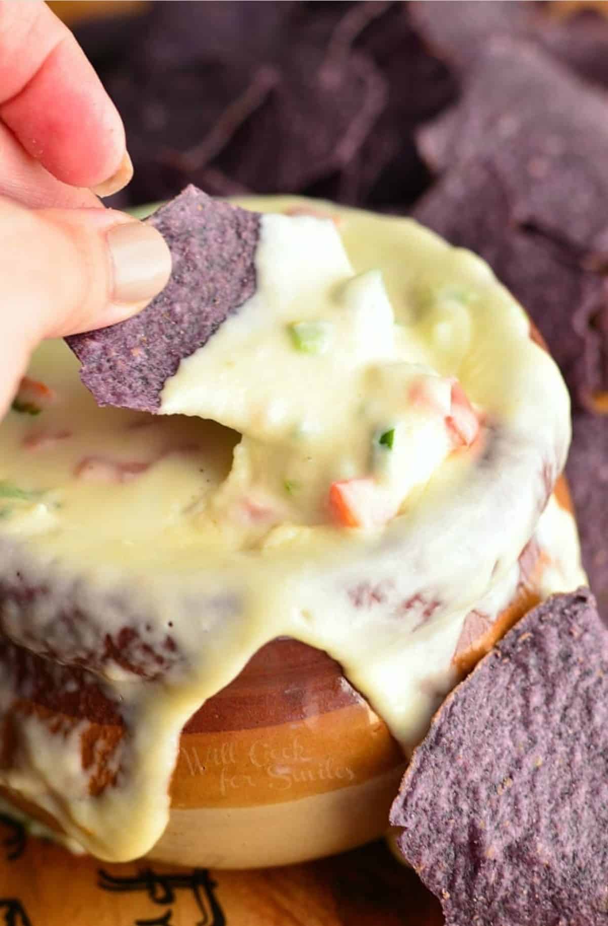 dipping into a queso dip with blue tortilla chips and more around the pot.