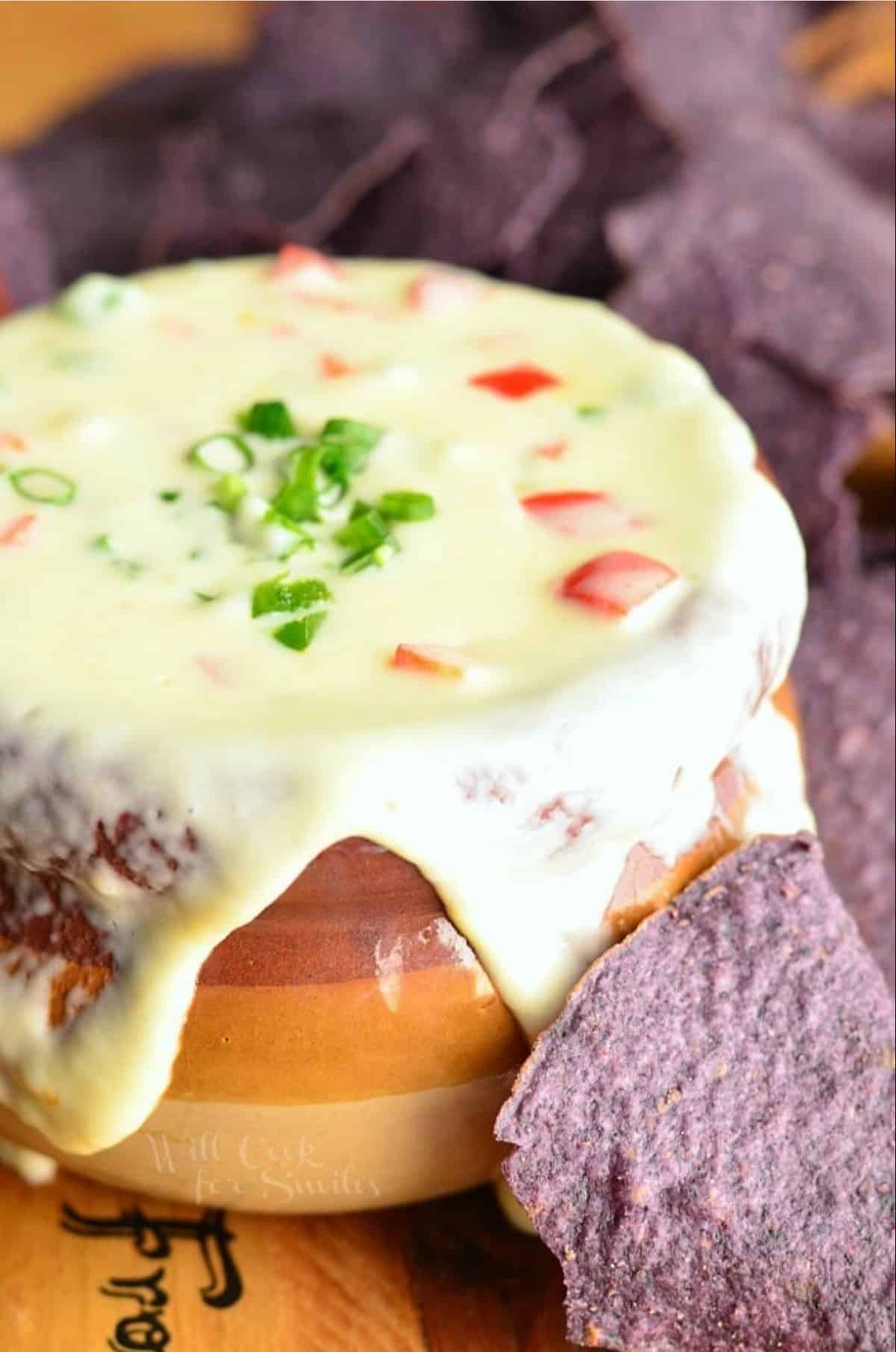 queso blanco full and overflowing in a brown crock with blue tortilla chips around.